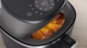 Zwarte Philips Airfryer met een kijkvenster waar goudbruine kipstukken in zichtbaar zijn.