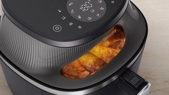Zwarte Philips Airfryer met een kijkvenster waar goudbruine kipstukken in zichtbaar zijn.