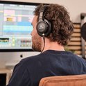 Man met krullend bruin haar draagt een zwarte Devine PRO 4000 hoofdtelefoon tijdens het werken op een computer.