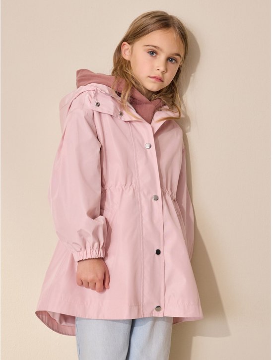 Meisje draagt een roze regenjas met capuchon en drukknopen over een bordeauxrode hoodie.
