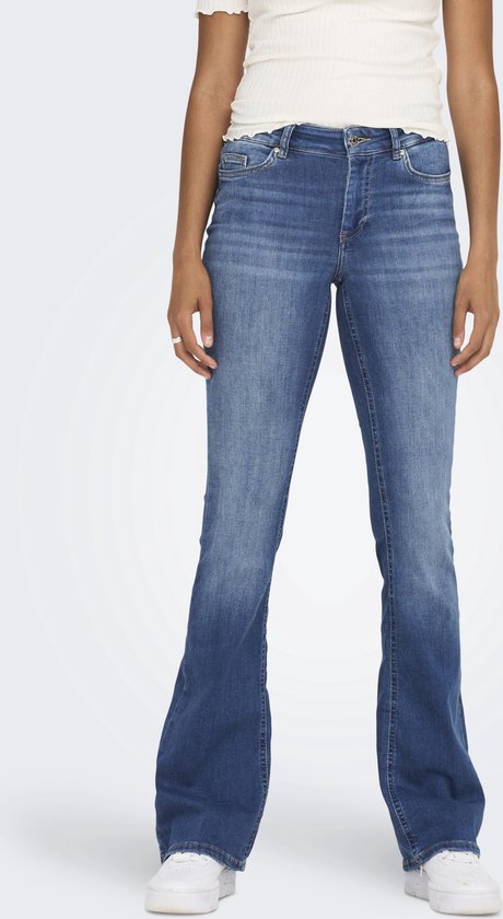 Model in een spijkerbroek met wijde pijpen in een medium denim wassing, met witte sneakers.