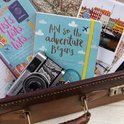 Reisdagboek "And so the adventure begins..." met wereldkaart, camera en paspoort.