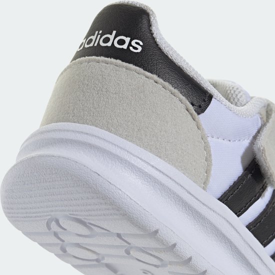 Detail van de hiel van een witte kindersneaker met een suède overlay, zwart detail met Adidas-logo en witte zool.
