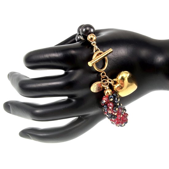 Armband met gouden hartbedel en rode en zwarte kristallen bedel aan een schakel, gedragen op een zwarte etalagehand.