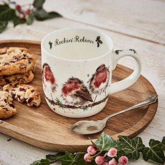 Witte mok met drie schattige roodborstjes op een tak, op een houten schaal met koekjes en hulst.