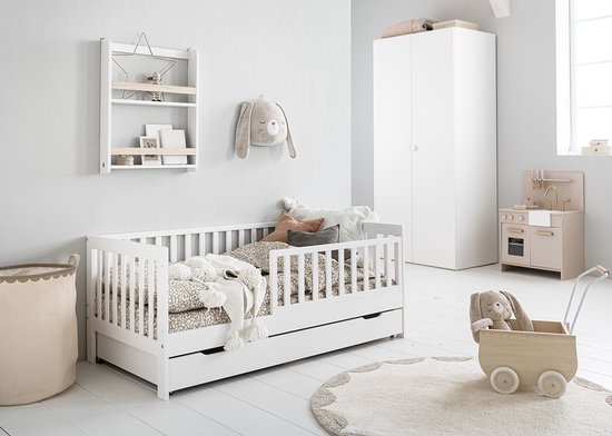Wit kinderbed met lade, dekens en kussens. Een houten poppenwagen met konijn ernaast.