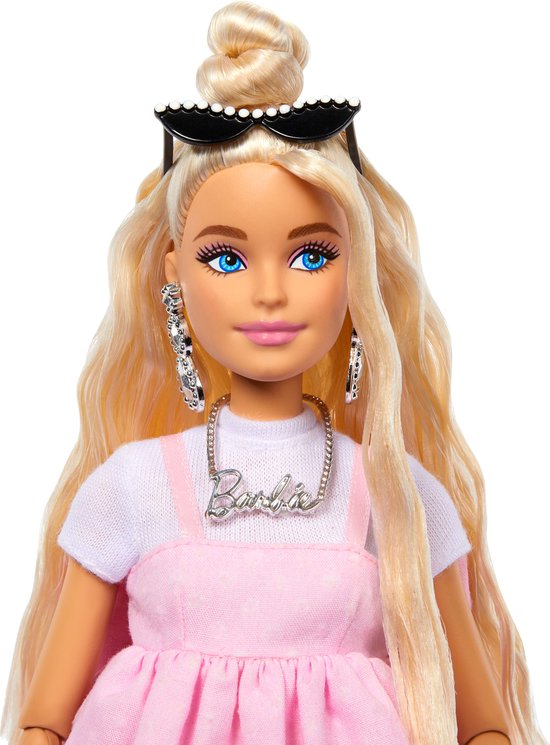 Close-up van Barbiepop met blonde staart, blauwe ogen, ketting met 'Barbie'-opschrift, grote oorbellen.