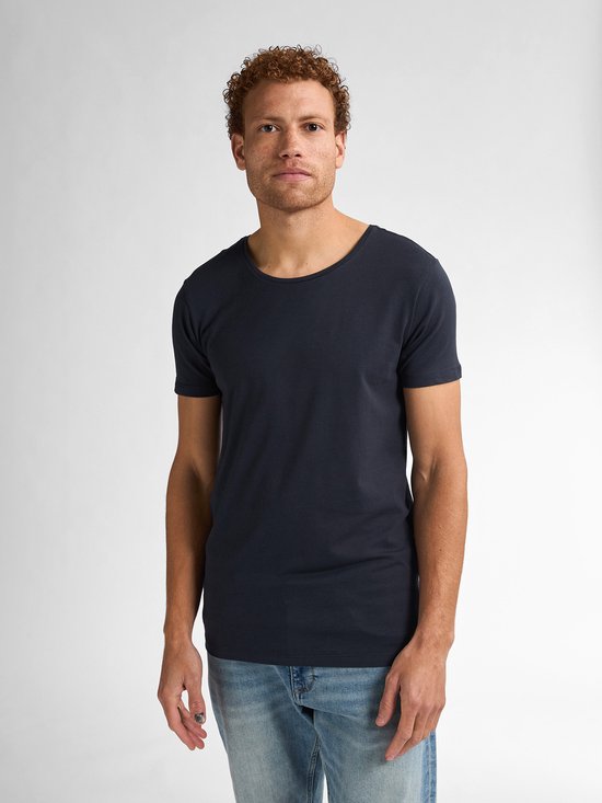 Model met krullend rood haar, sproeten, donkerblauw t-shirt en lichte spijkerbroek.