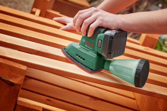 Groene Bosch multischuurmachine in gebruik op een houten ligstoel. Stofopvangbak is bevestigd.