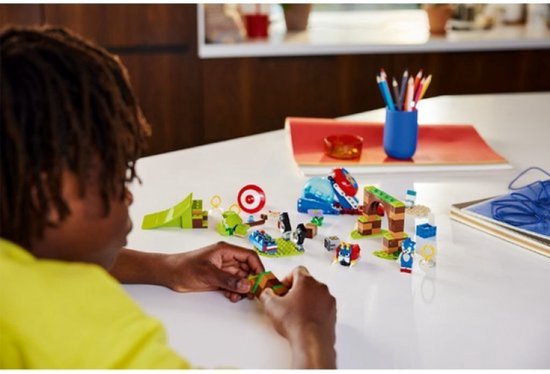 Een jongen met een gele trui die een LEGO Sonic speelset bouwt met Sonic, een lanceerbaan en hindernissen.