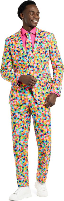 Man in een volledig pak met confettiprint en roze overhemd, witte sneakers.