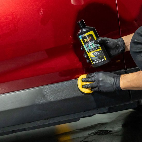 Hand in zwarte handschoen brengt Meguiar's Ultimate Black Plastic Restorer aan op zwarte kunststof auto-onderdeel.