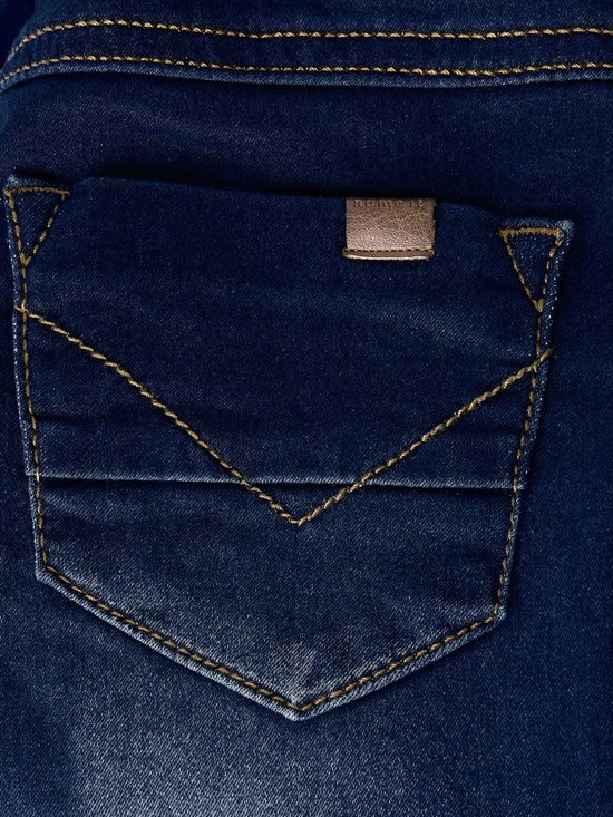 Detail van een achterzak van een donkerblauwe spijkerbroek met stonewashed effect, oranje V-stiksels en een merklabel.