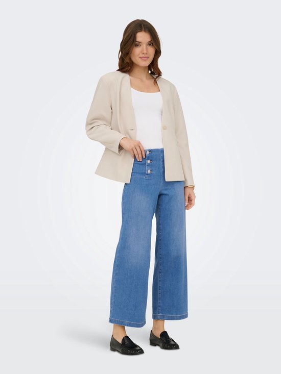 Model in lichtblauwe spijkerbroek met hoge taille, wijde pijpen en vier knopen, met beige blazer.