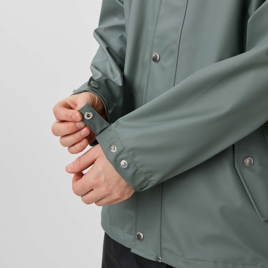 Gedetailleerde opname van de mouw van een groene jas, die een drukknoop sluit.