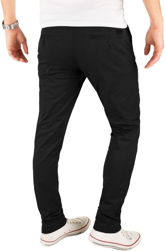 Achterkant van een man met een zwarte slim fit chinobroek, witte t-shirt en witte sneakers. De broek heeft twee knopen op de achterzakken.