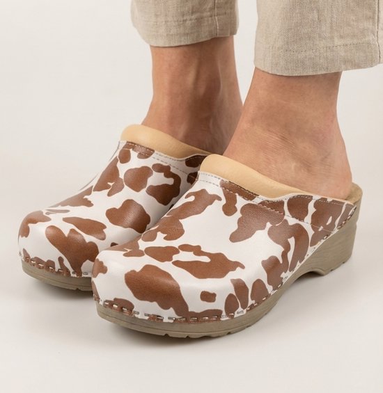 Voeten in beige klompen met bruine koeienvlekkenprint en beige leren rand. Beige zool.