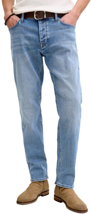 Man in een lichtblauwe jeans, witte top, bruine riem en beige laarsjes.