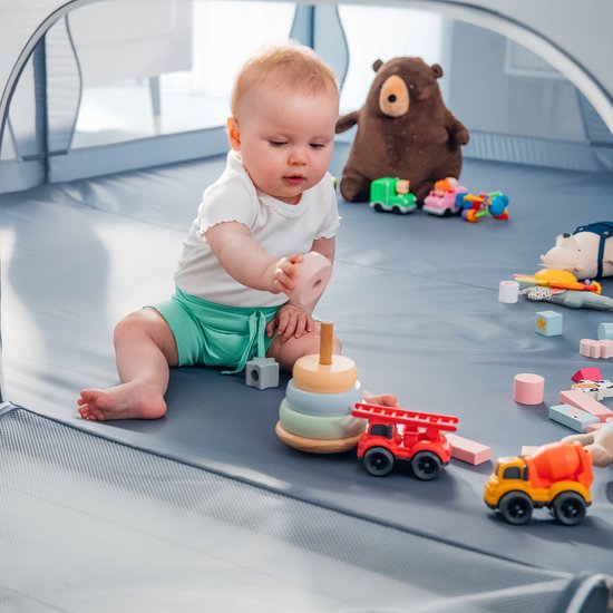 Baby speelt met houten speelgoed in een grijze box met een berenspeeltje.