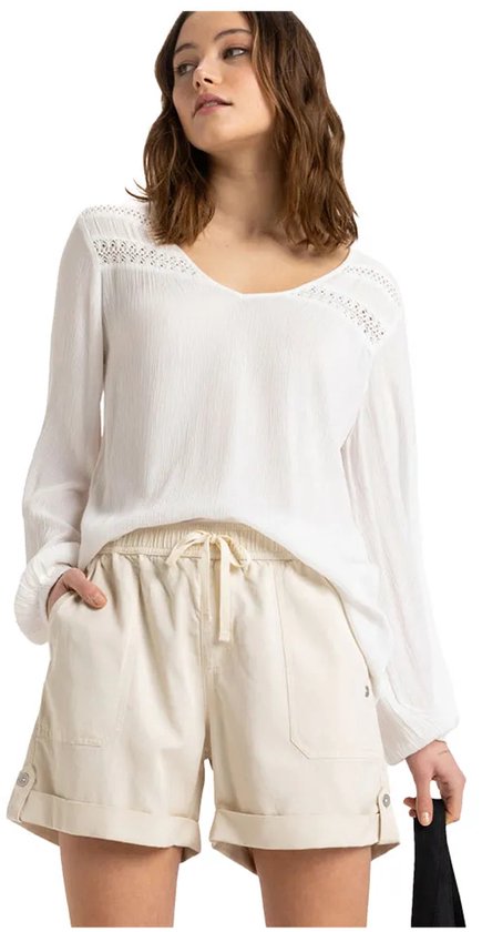 Model in een crème kleurige korte broek met ceintuur en een witte blouse met wijde mouwen.