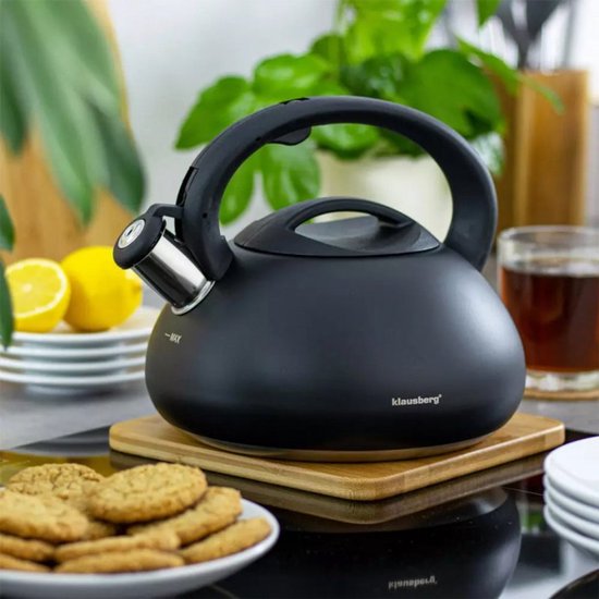Zwarte Klausberg fluitketel op een houten onderzetter, met citroenen, koekjes en thee.