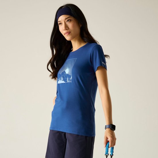 Vrouw draagt blauw Regatta sportshirt met korte mouwen en berggrafiek op de borst, gecombineerd met donkerblauwe short.