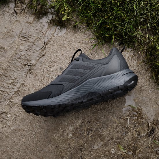 Zwarte Adidas Terrex trailrunningschoen op een modderige ondergrond met gras.