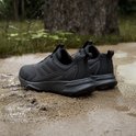 Paar zwarte Adidas Terrex trailrunningschoenen op een modderige ondergrond, achterkant van de schoenen te zien.