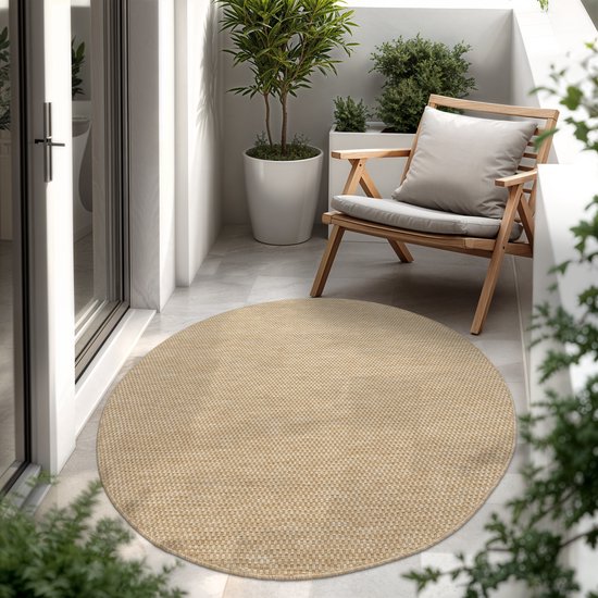 Rond beige kleed op een balkon met houten stoel, kussen, planten en glazen deur.