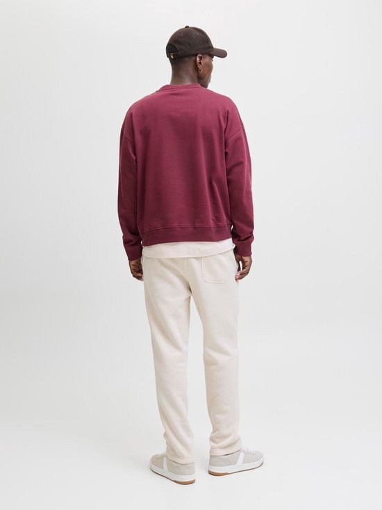 Man in crème joggingbroek en bordeaux hoodie, van achteren gezien.