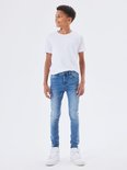 Jongensmodel in een witte t-shirt en een skinny spijkerbroek van medium blue denim.