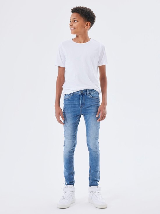 Jongensmodel in een witte t-shirt en een skinny spijkerbroek van medium blue denim.