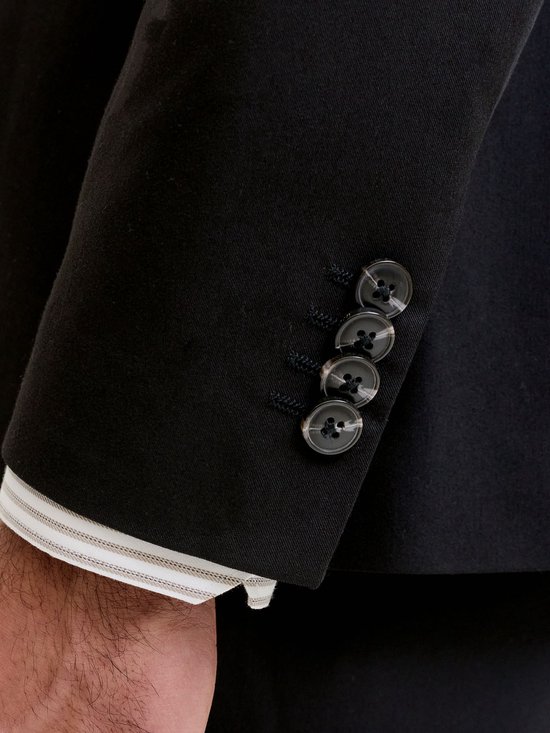 Close-up van de knopen op de mouw van een zwart colbert met gestreepte manchet.