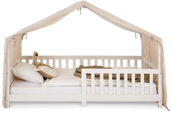 Wit kinderbed met een beige hemel met pompons en decoratieve lussen. Met beddengoed en knuffel.