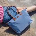 Blauwe nylon tas met bruine leren handvatten, liggend op het zand bij zonnig weer.