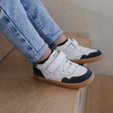 Kind draagt witte leren sneakers met donkerblauwe suède details en bruine zolen.