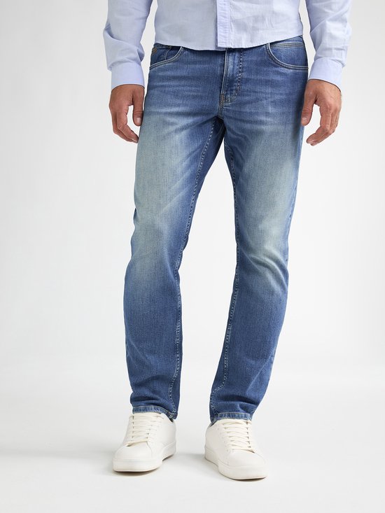 Mannelijke benen gedragen in een lichtblauwe spijkerbroek, met witte sneakers. De spijkerbroek heeft een gemiddelde wassing en een logo op de zak.