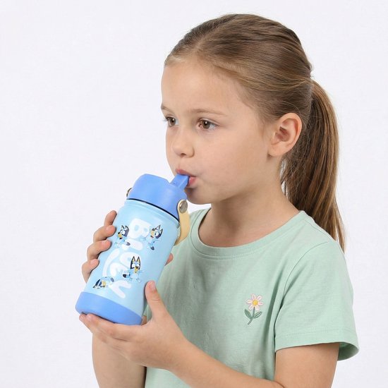 Een jong meisje met een paardenstaart drinkt uit een lichtblauwe waterfles met Bluey-print.