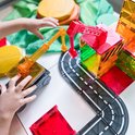Kinderhanden spelen met Magna-Tiles constructiespeelgoed, inclusief een hijskraan, wegen en kleurrijke transparante bouwblokken.