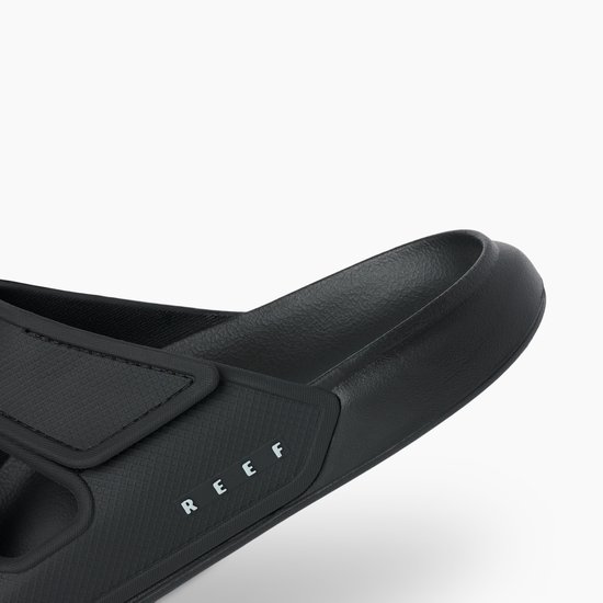 Close-up van de neus van een zwarte Reef slipper met een dikke zool en klittenbandsluiting.
