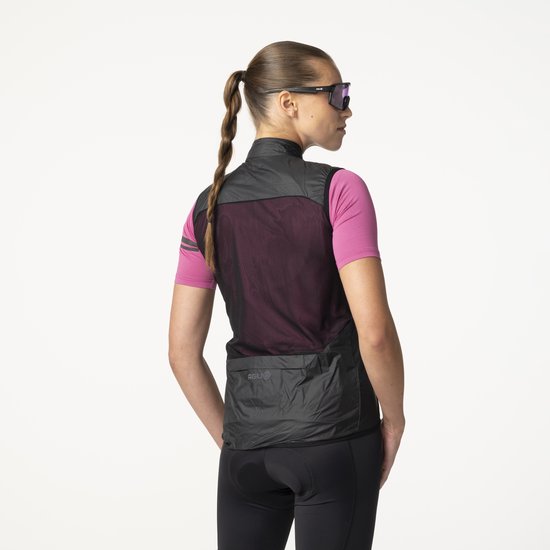 Vrouw in roze fietsshirt, zwarte bodywarmer met mesh achterkant en zonnebril, van achteren gezien.