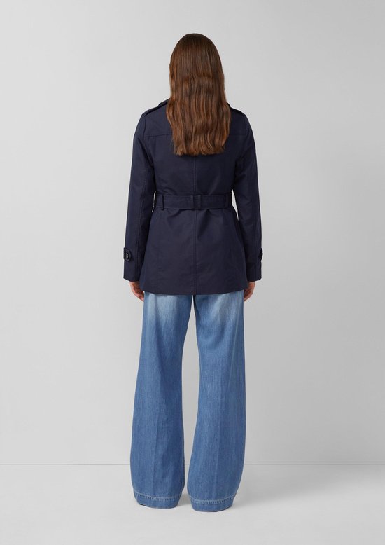 Achterkant van een model in donkerblauwe trenchcoat met ceintuur en wijde jeans.