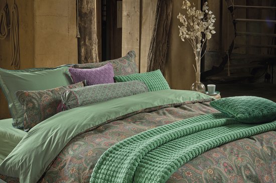 Bed opgemaakt met groene lakens, kussens en een dekbedovertrek met paisley print.