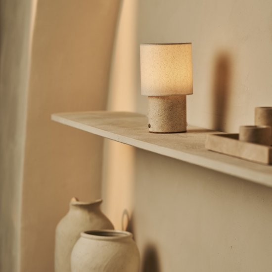 Kleine beige tafellamp met linnenkap en travertijnen voet, staand op een plank.