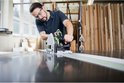 Homme avec lunettes de sécurité et protection auditive utilise une scie plongeante Festool TS 55 FEBQ sur un établi.