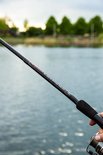 Hand houdt een 'Ultimate Allround Power Feeder' hengel vast boven water.