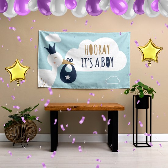 Een feestelijke backdrop in een kamer met ballonnen en planten. De backdrop toont een ooievaar met "HOORAY IT'S A BOY" tekst.