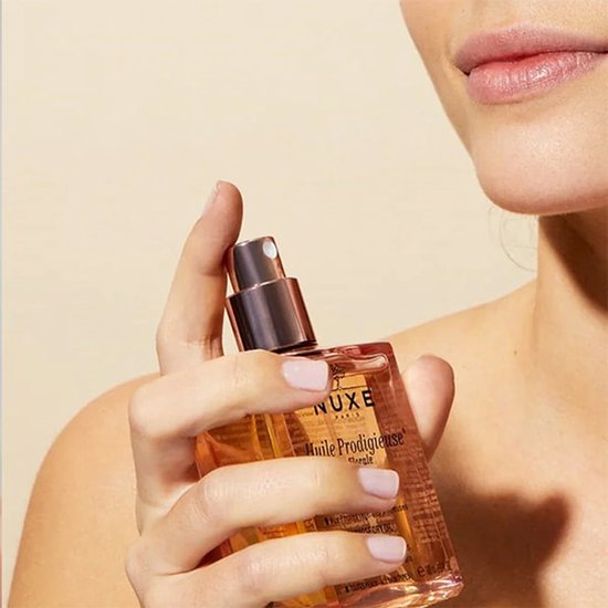 Vrouw met lichte huid houdt een fles Nuxe Huile Prodigieuse multi-purpose dry oil met gouden dop.