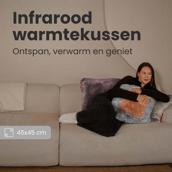 Een vrouw zit op een bank en houdt een grijs bontkussen met oranje gloeiend honingraatpatroon vast. Tekst: "Infrarood warmtekussen".