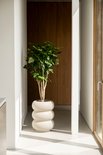 Een grote plantenbak in off-white met een bolvormig, gestapeld design met een groene plant, in een moderne hal.